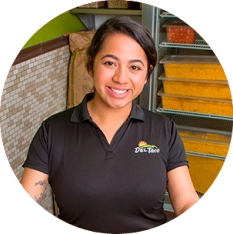 Portrait photo of a Del Taco Shift Manager. She is holding food prep container and wears a branded Del Taco polo.