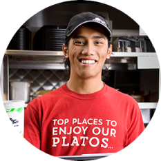 Portrait photo of a Del Taco Team Member infront of the register. He is wearing a work shirt that reads: Top places to enjoy our platos.