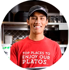 Portrait photo of a Del Taco Team Member infront of the register. He is wearing a work shirt that reads: Top places to enjoy our platos.